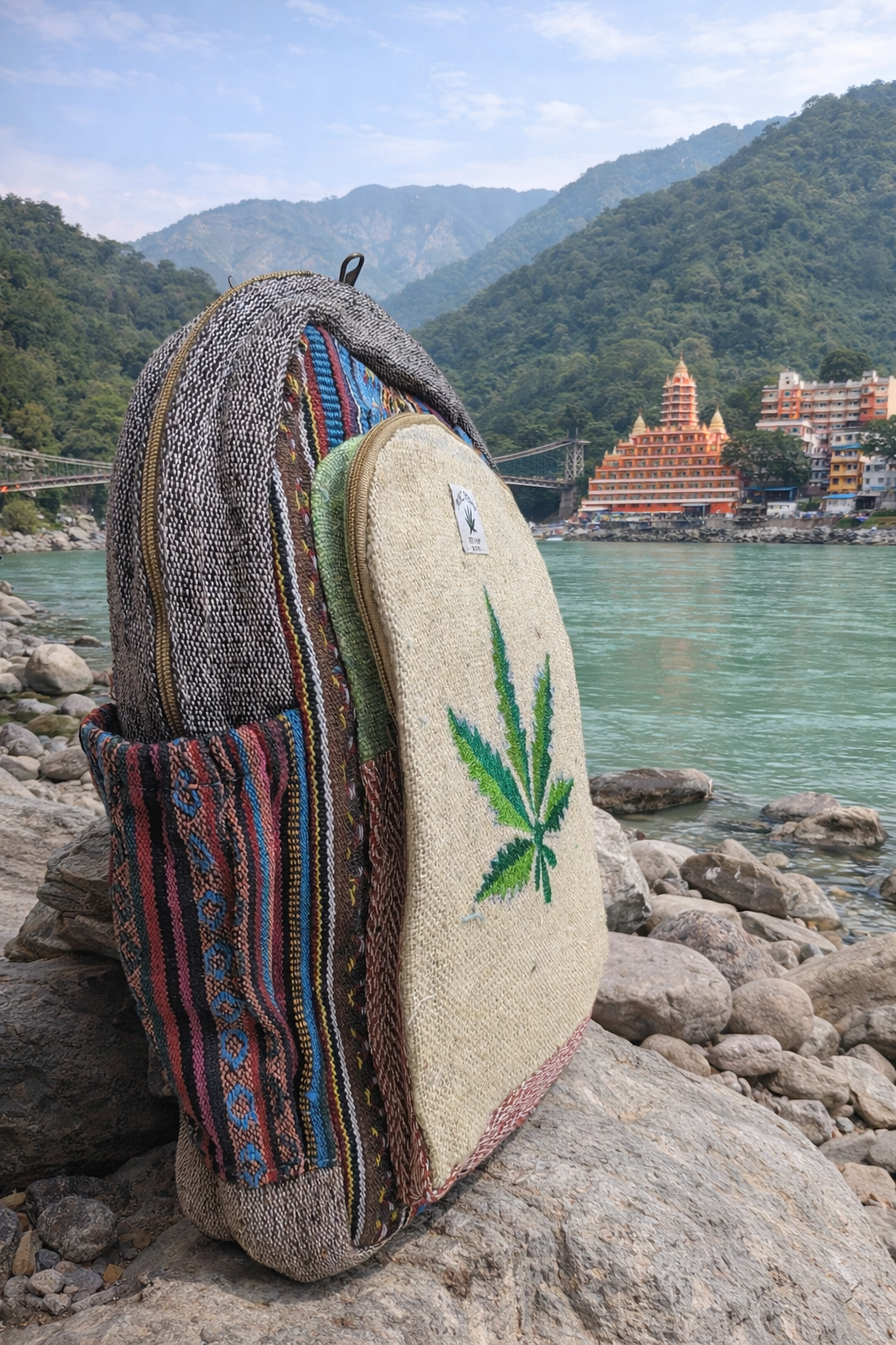Backpack with cannabis leaf design on a rocky shore with mountains and a temple in the background