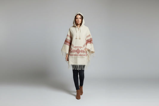 Woman wearing a cream-colored hooded poncho with red patterns on a gray background