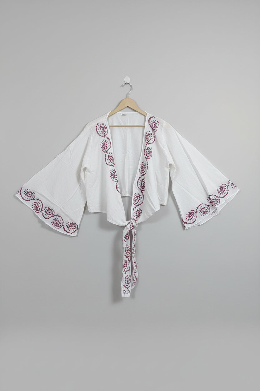 White embroidered garment on a hanger against a plain wall.
