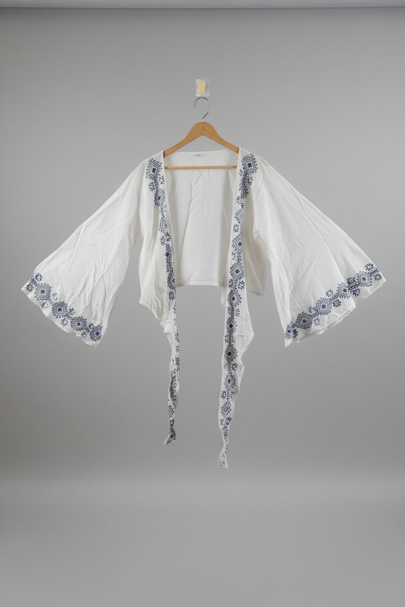 White garment with blue embroidery on a hanger against a white wall.