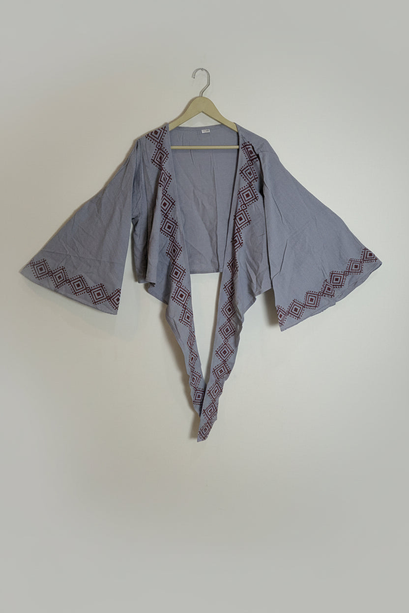 Gray embroidered jacket on a hanger against a white wall.