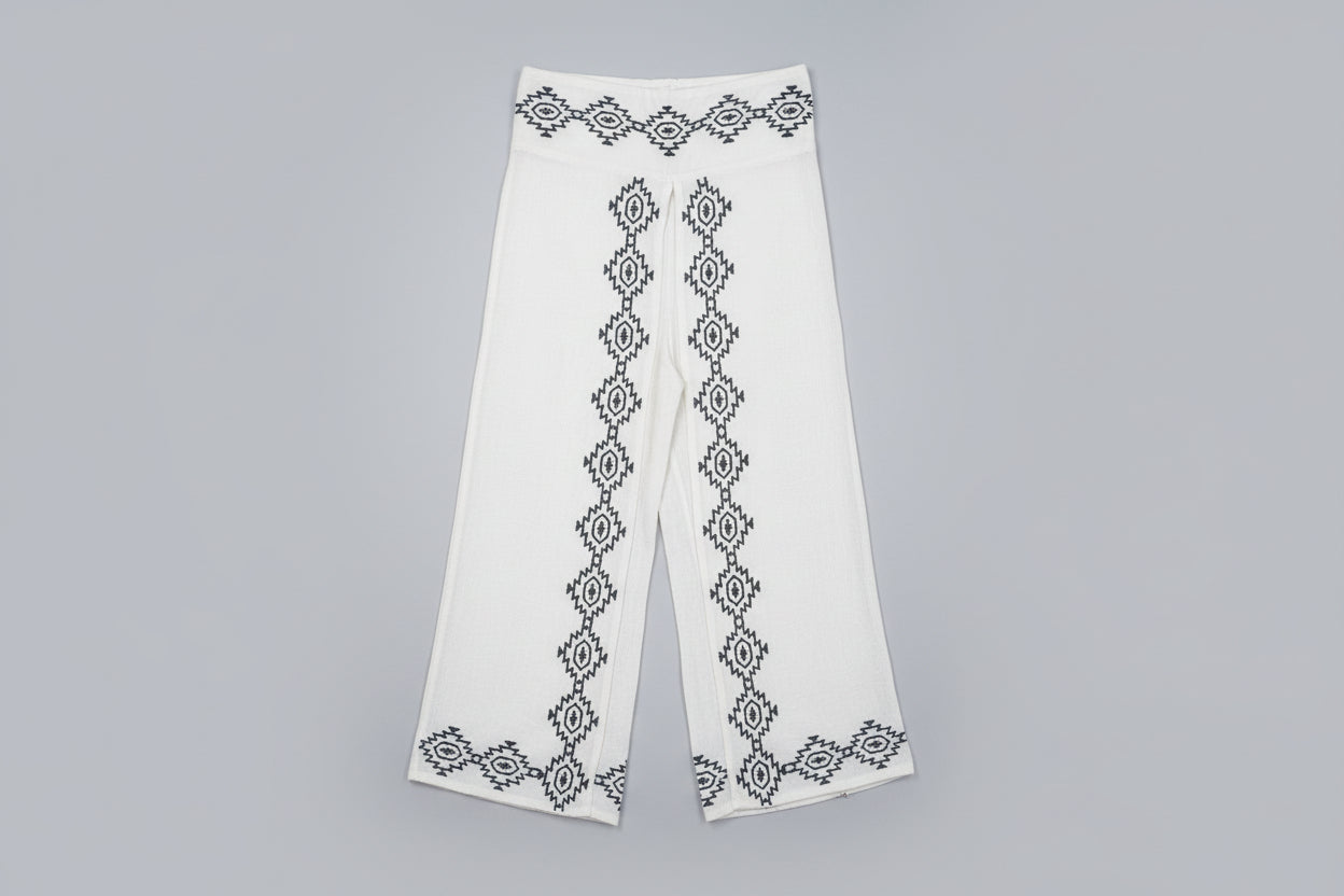 White garment with black embroidery on a hanger against a white wall.