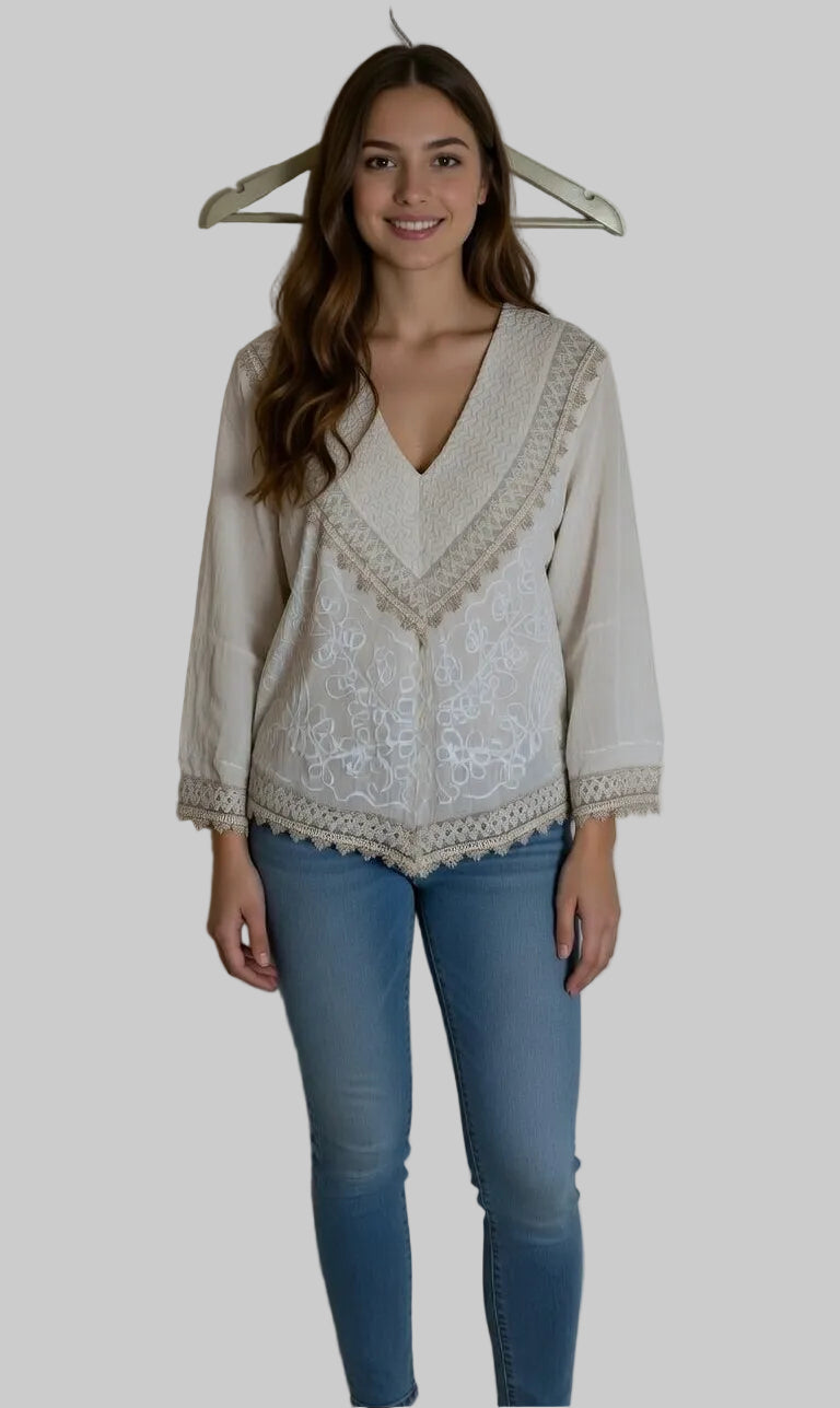 Woman wearing a white blouse with lace details and blue jeans against a plain background